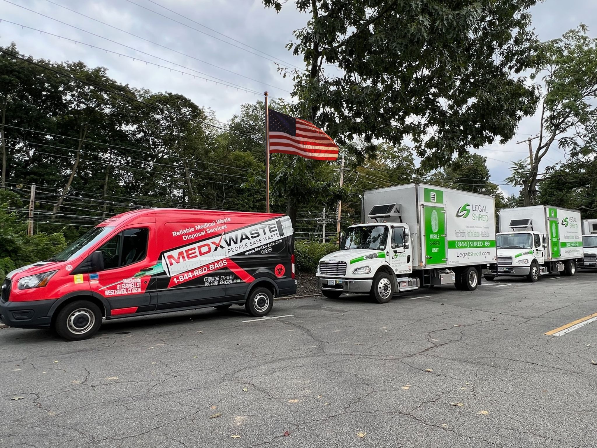 Red MedX Waste Medical Waste Disposal Van Parked Next To Two Legal Shred Mobile Shred Unit Trucks Under An American Fl