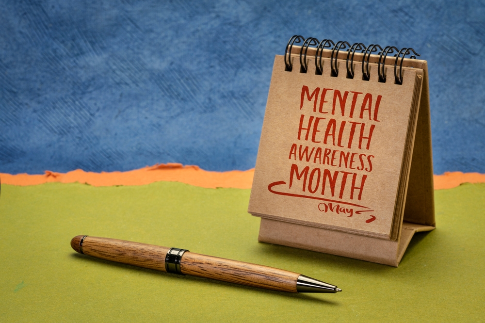 Desk Calendar Displaying 'Mental Health Awareness Month May' Next To A Wooden Pen On A Green Surface With A Blue And O