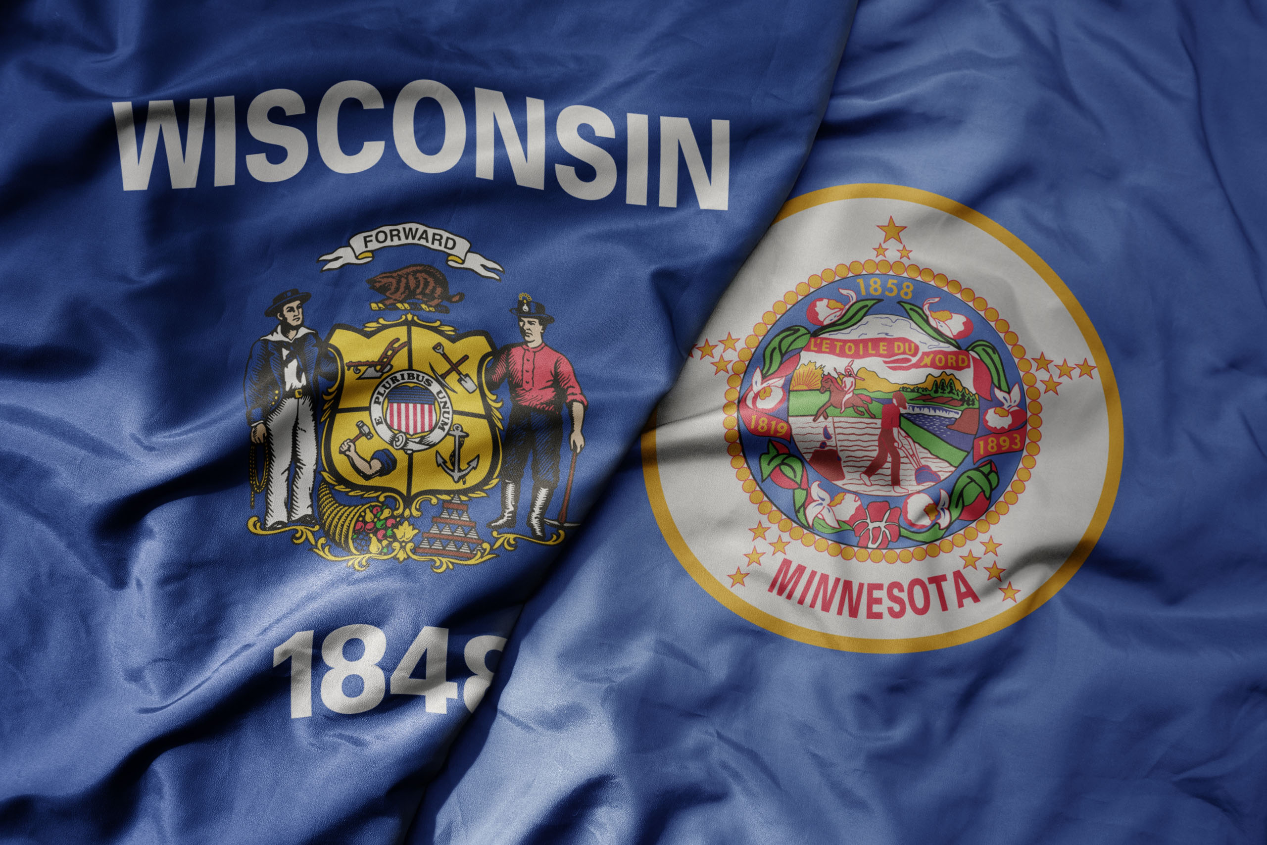Close-Up Of The Wisconsin State Flag Next To The Minnesota State Flag, Both Showing Detailed State Seals On A Blue Bac